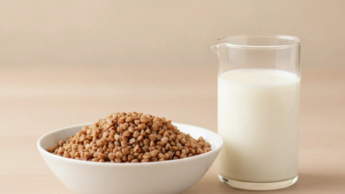 A bowl of loose cooked buckwheat and a glass of kefir side by side on a light table