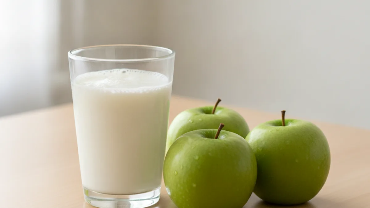 A glass of kefir and three green apples on a light-colored table